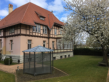 Das Haus der Landeszentrale vom Garten aus gesehen. Rechts ist der blühende Kirschbaum zu sehen, links daneben ein kleiner Pavillon.